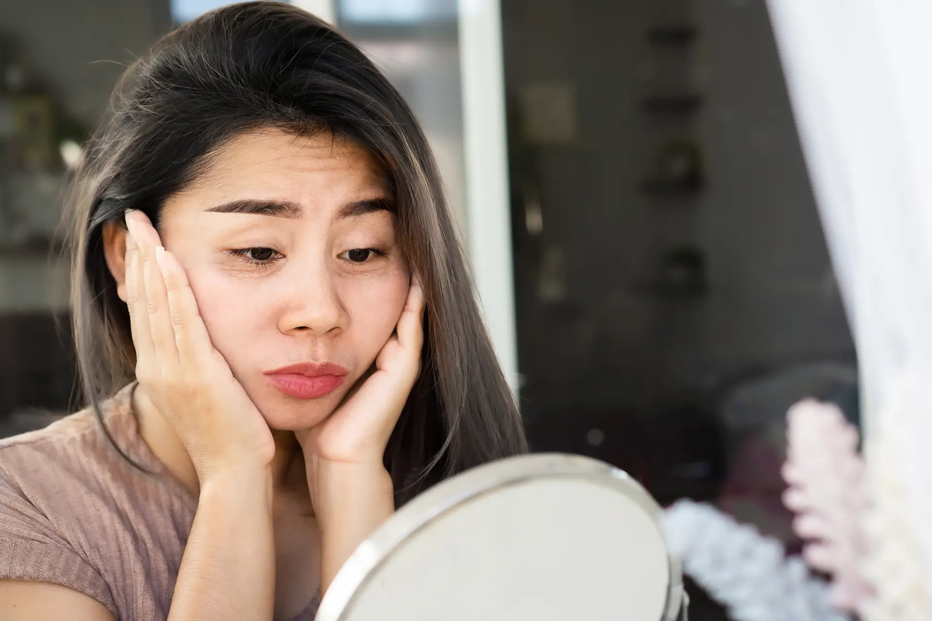 A young woman notices signs of fatigue, tension, or imbalance in her skin.